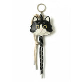 Front view of a custom handmade leather keychain of a black and white cat on a white background.