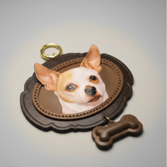 A high-quality studio shot of the custom pet portrait leather keychain, highlighting the detailed texture, stitching, and the lifelike portrait of a Chihuahua dog. The matching bone charm and gold clasp are also visible.
