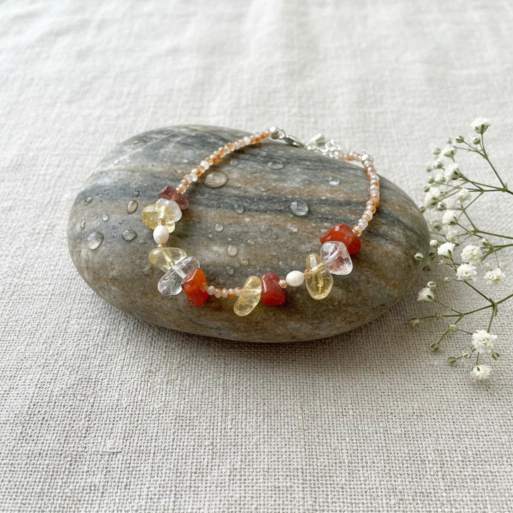 A natural style pet-and-owner bracelet or necklace made from raw gemstones like carnelian and citrine, displayed on a wet pebble.