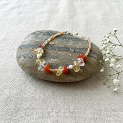 A natural style pet-and-owner bracelet or necklace made from raw gemstones like carnelian and citrine, displayed on a wet pebble.
